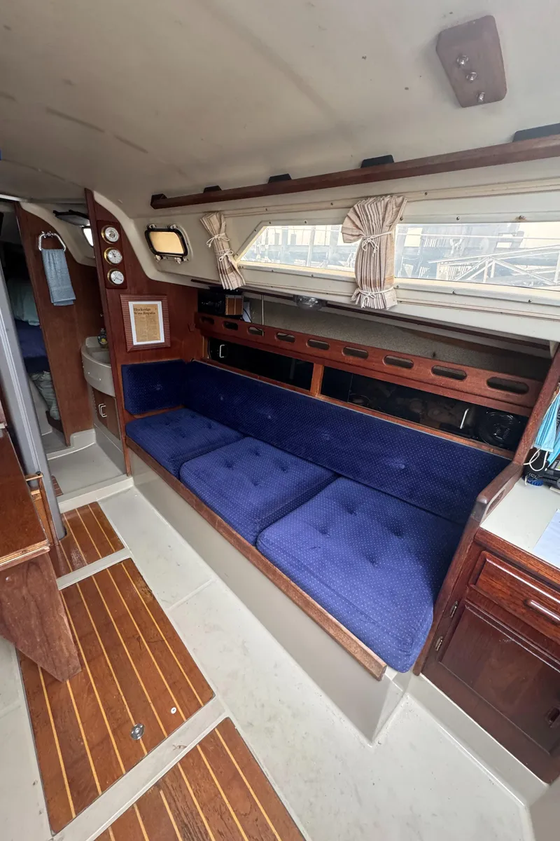Slide: The Image of Interior of a 1985 O'Day Sloop sailboat with blue cushioned seating and wooden accents. - 11