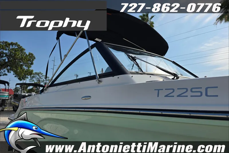 Slide: The Image of 2025 Trophy T22 SC boat with tan seating, windshield, and black canopy at a marina. - 82