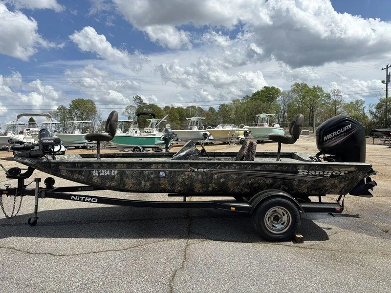 Slide: The Image of 2015 Ranger RC188 fishing boat on trailer, camo design, Mercury outboard motor, parked outdoors. - 14