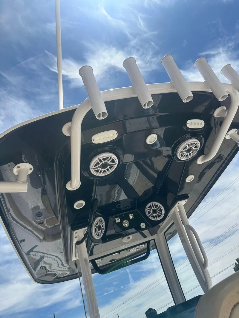 Slide: The Image of 2023 Sportsman Masters 247OE Bay Boat, underside view with rod holders and speakers against blue sky. - 19