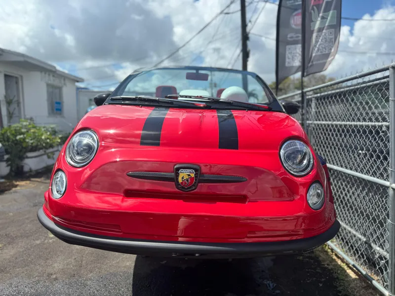 Slide: The Image of Red 2025 Fiat 500 Abarth with black racing stripes, parked outdoors. - 2