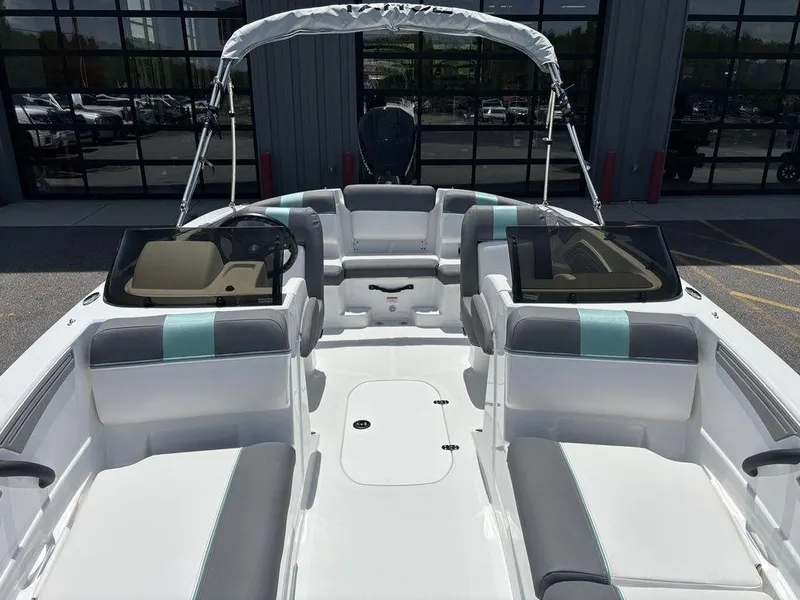 Slide: The Image of 2025 Tahoe T21 boat interior with seating, windshield, and canopy, parked outside a building. - 12