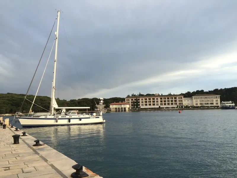 Slide: The Image of Sailboat Hallberg-Rassy 48 (2006) docked at a serene marina with buildings in the background. - 2