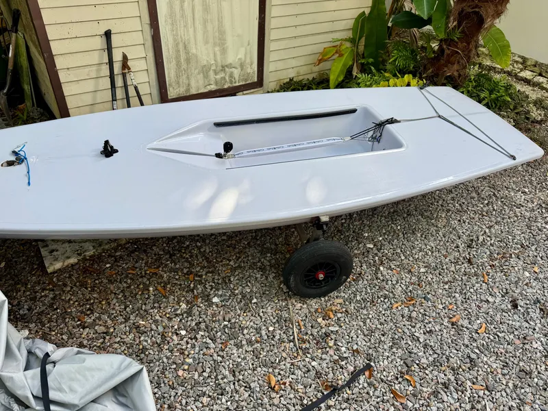 Slide: The Image of 2023 Dinghy PSA ILCA 6 on gravel, near plants and a wooden structure. - 2