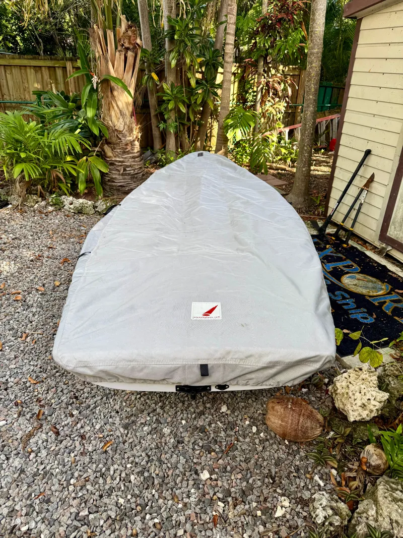 Slide: The Image of 2023 Dinghy PSA ILCA 6 covered, resting on gravel near tropical plants. - 4