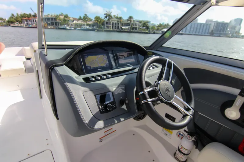 Slide: The Image of 2021 Cobalt 25SC boat dashboard with steering wheel and navigation screens, overlooking waterfront homes. - 40