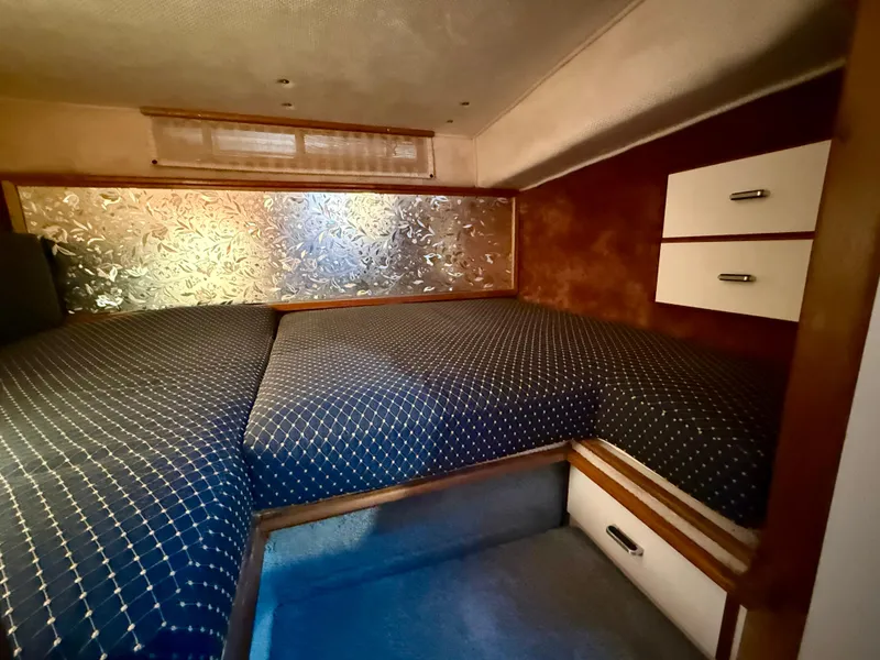 Slide: The Image of 1989 Sea Ray 340 Sundancer cabin with patterned bedding and wooden storage drawers. - 6