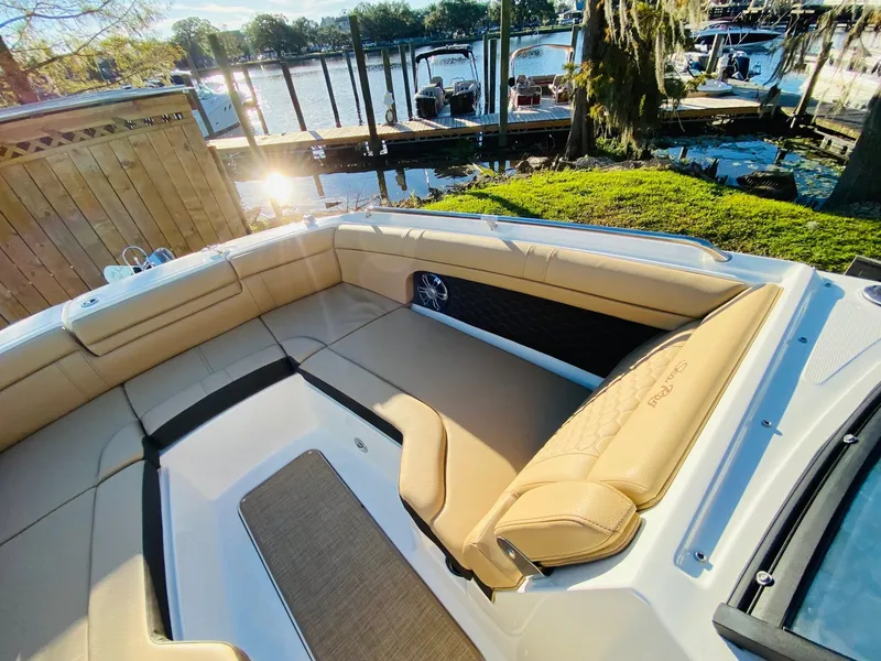 Slide: The Image of 2022 Sea Ray 270 SDX boat interior with tan seating, docked by a scenic waterfront. - 22