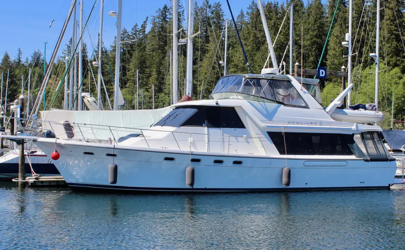 The Image of 1999 Bayliner 4788 Motoryacht docked in a marina, surrounded by trees and sailboats. - 1