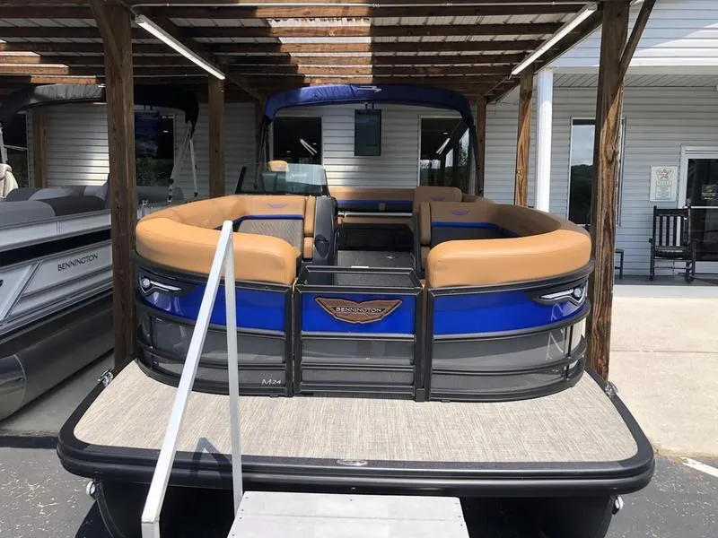 Slide: The Image of 2025 Bennington M L-Bench 24ML pontoon boat with blue and tan seating, docked under a pergola. - 2