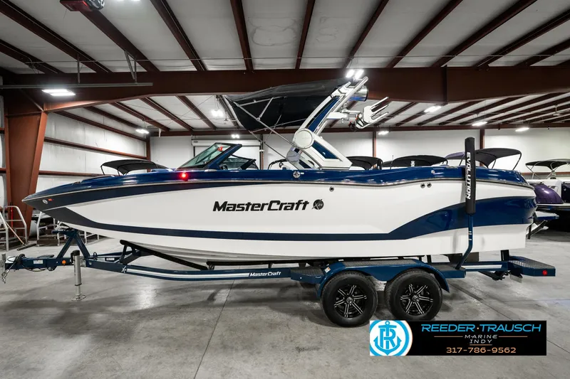 Slide: The Image of 2025 MasterCraft X24 boat in showroom, blue and white design, on trailer. - 11