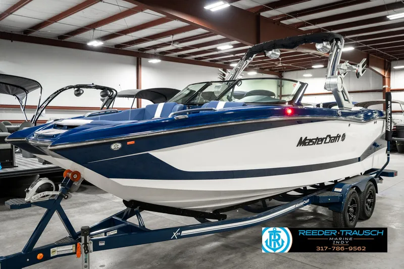 Slide: The Image of 2025 MasterCraft X24 boat in showroom, blue and white design on trailer. - 2