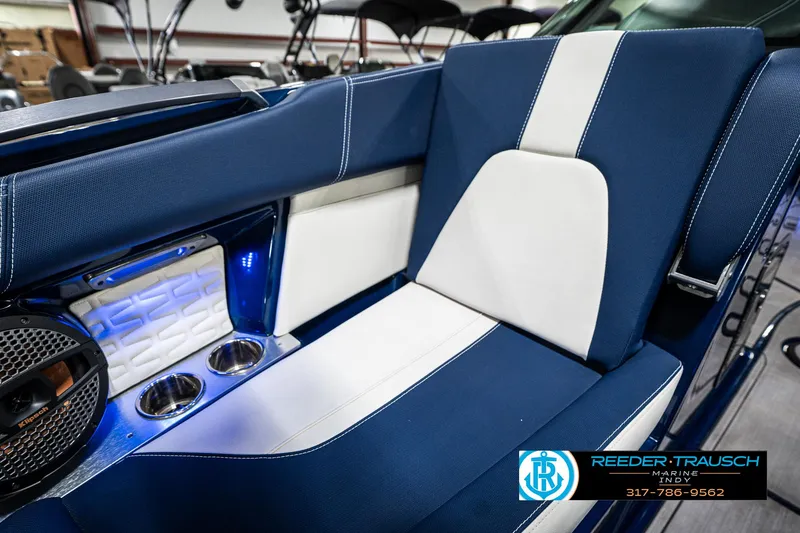 Slide: The Image of 2025 MasterCraft X24 boat interior with blue and white seating, cup holders, and speaker. - 48
