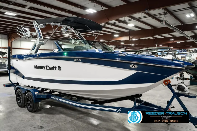 Slide: The Image of 2025 MasterCraft X24 boat in showroom, blue and white design, on trailer. - 6
