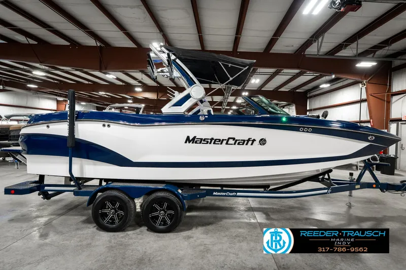 Slide: The Image of 2025 MasterCraft X24 boat in showroom, blue and white design, on trailer. - 7