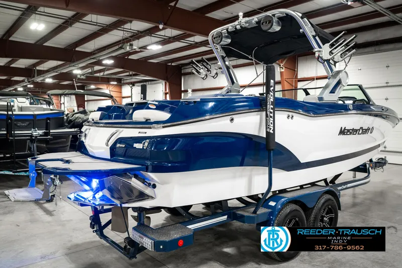 Slide: The Image of 2025 MasterCraft X24 boat in showroom, blue and white design, on trailer. - 8