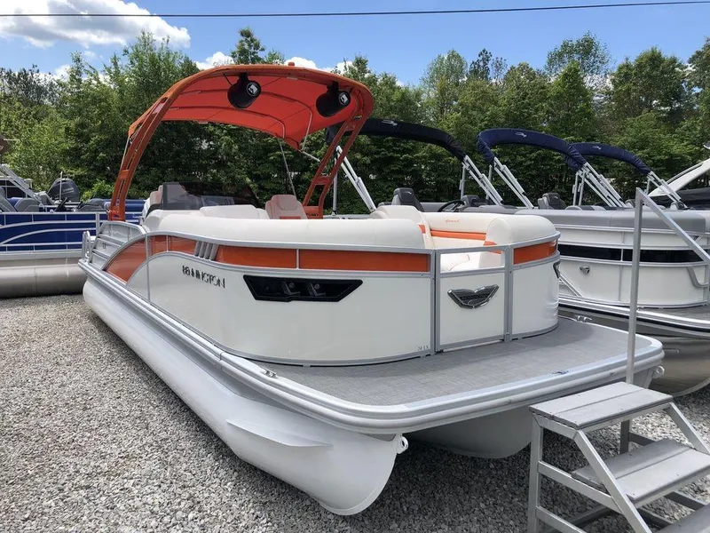 Slide: The Image of 2024 Bennington 24 LXSSBA pontoon boat with orange canopy, parked on gravel. - 1