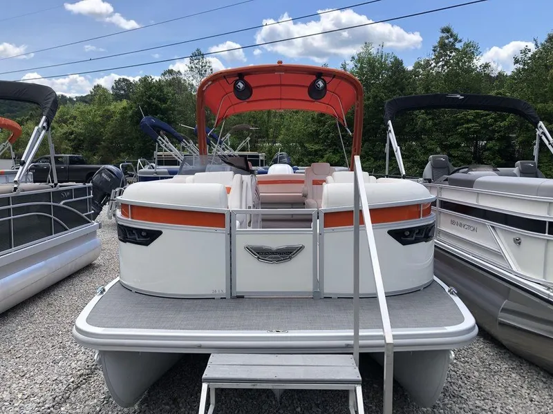 Slide: The Image of 2024 Bennington 24 LXSSBA pontoon boat with orange canopy, docked on gravel lot. - 3