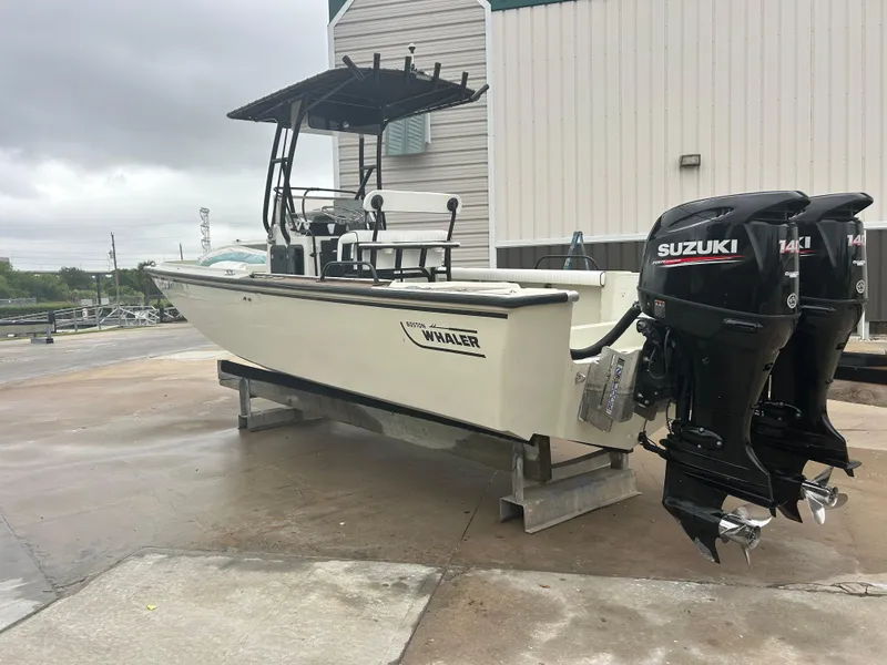 Slide: The Image of 1983 Boston Whaler 25 Outrage boat with dual Suzuki engines, parked outdoors. - 2
