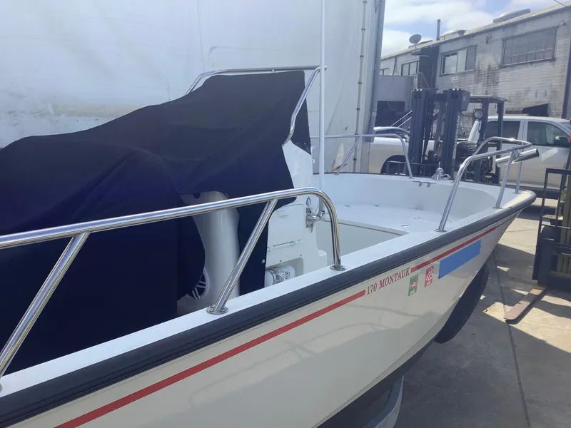 Slide: The Image of 2022 Boston Whaler 170 Montauk boat docked, partially covered, in an industrial setting. - 3