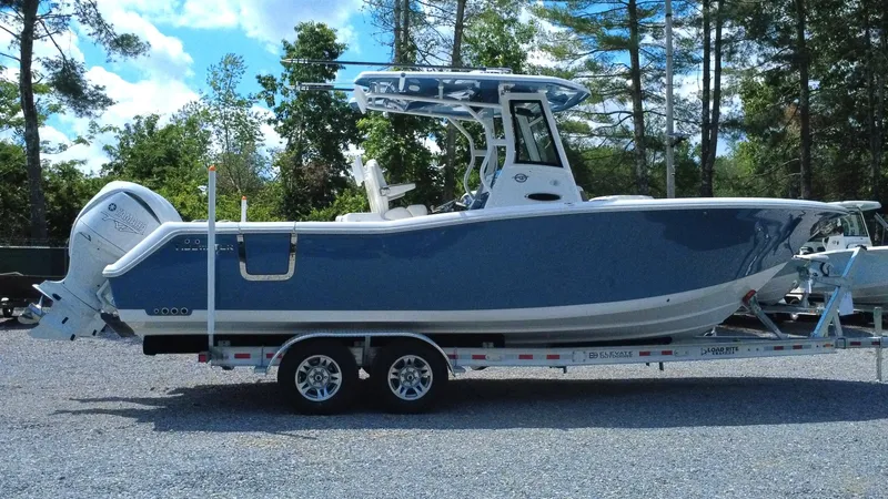 Slide: The Image of 2025 Tidewater 282 CC Adventure boat on trailer, parked outdoors with trees in background. - 9