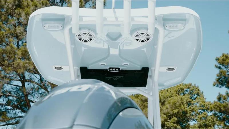 Slide: The Image of 2025 Tidewater 210 LXF boat with speakers and canopy, viewed from below against a tree backdrop. - 34