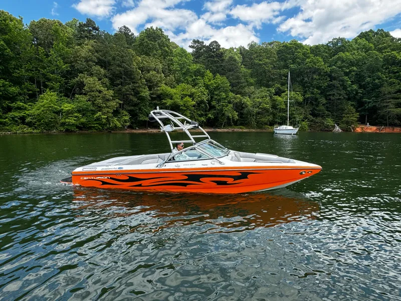 Slide: The Image of 2007 Centurion Avalanche boat with orange flame design on a lake, surrounded by lush trees. - 2