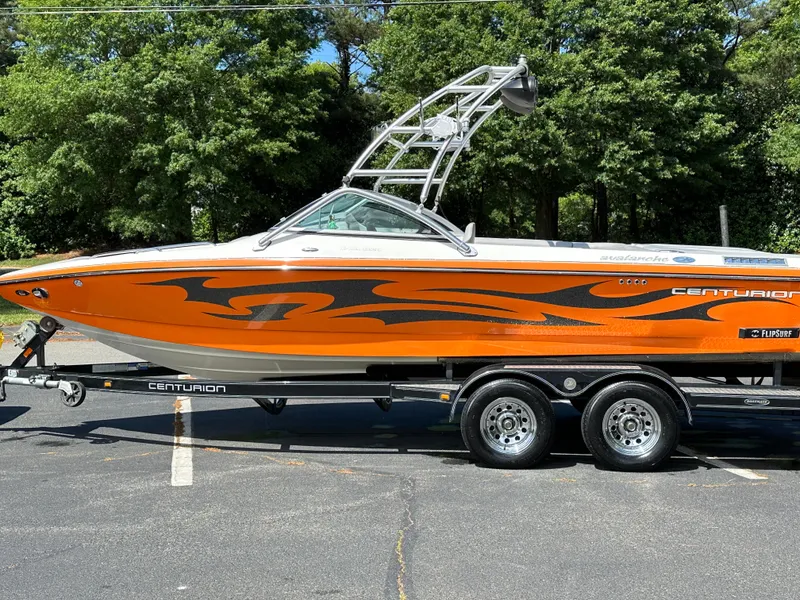 Slide: The Image of 2007 Centurion Avalanche boat with orange and black design on a trailer, parked outdoors. - 21