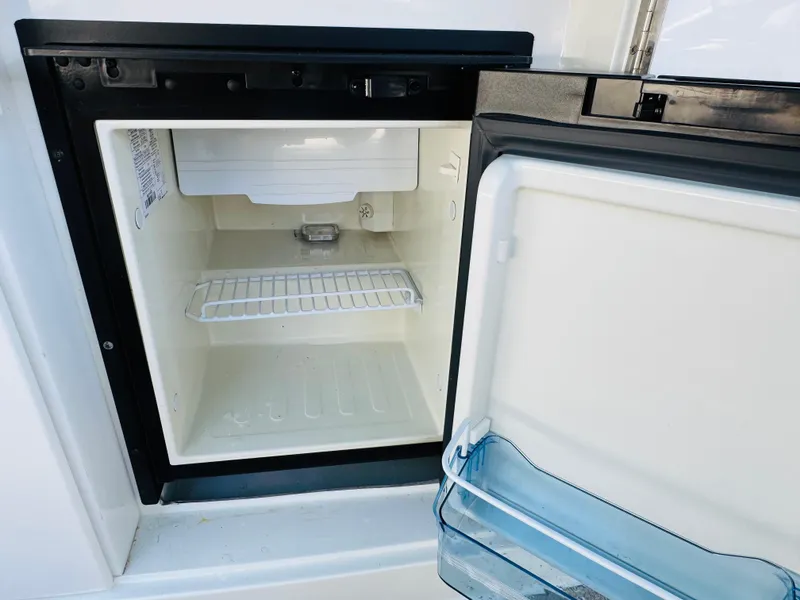 Slide: The Image of Open mini fridge on a 1998 Cobalt 293 boat, showing empty interior and door storage. - 25