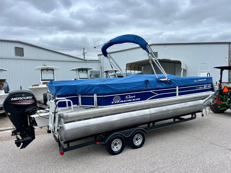 Slide: The Image of 2017 Sun Tracker Fishin' Barge 22 DLX pontoon boat with blue cover on trailer. - 25
