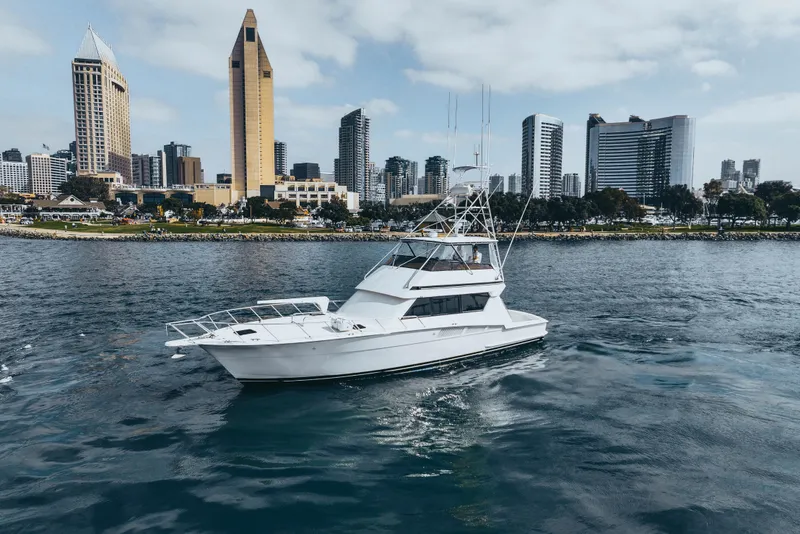 Slide: The Image of 1990 Hatteras 58 Convertible yacht cruising near city skyline, calm waters. - 1