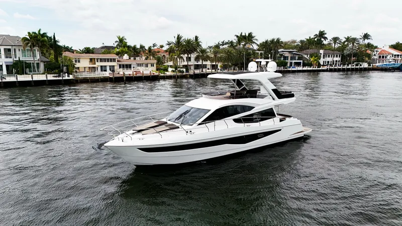Slide: The Image of 2020 Galeon 550 Fly yacht cruising on a scenic waterfront with luxury homes in the background. - 3