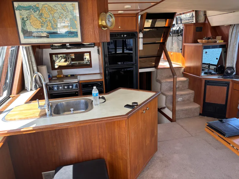 Slide: The Image of Interior of a 1994 Bayliner 4700 yacht with kitchen and stairs, featuring wood cabinetry. - 12