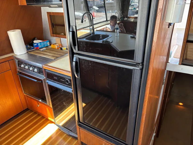 Slide: The Image of Bayliner 4700 yacht kitchen interior with stove, fridge, and sink, showcasing wood cabinetry, 1994 model. - 14