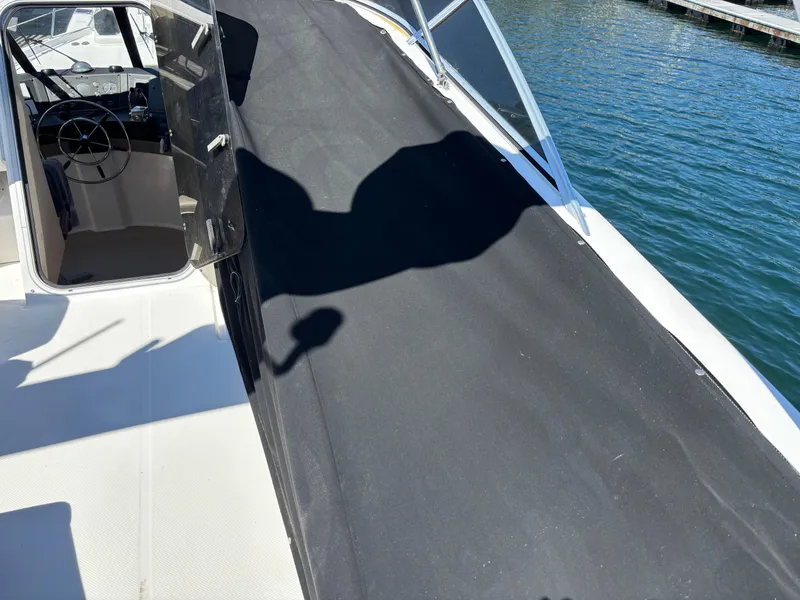 Slide: The Image of 1994 Bayliner 4700 boat deck with black cover, docked by the water. - 4