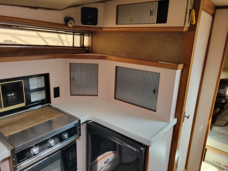 Slide: The Image of 1989 Sea Ray 340 Sundancer kitchen with stove, cabinets, and compact fridge. - 29