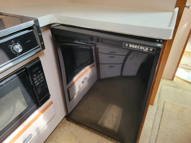 Slide: The Image of Compact kitchen area in a 1989 Sea Ray 340 Sundancer yacht, featuring a fridge and microwave. - 32