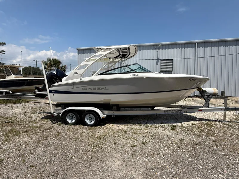 Slide: The Image of 2024 Regal LX2 boat on trailer, parked outdoors near a metal building. - 2