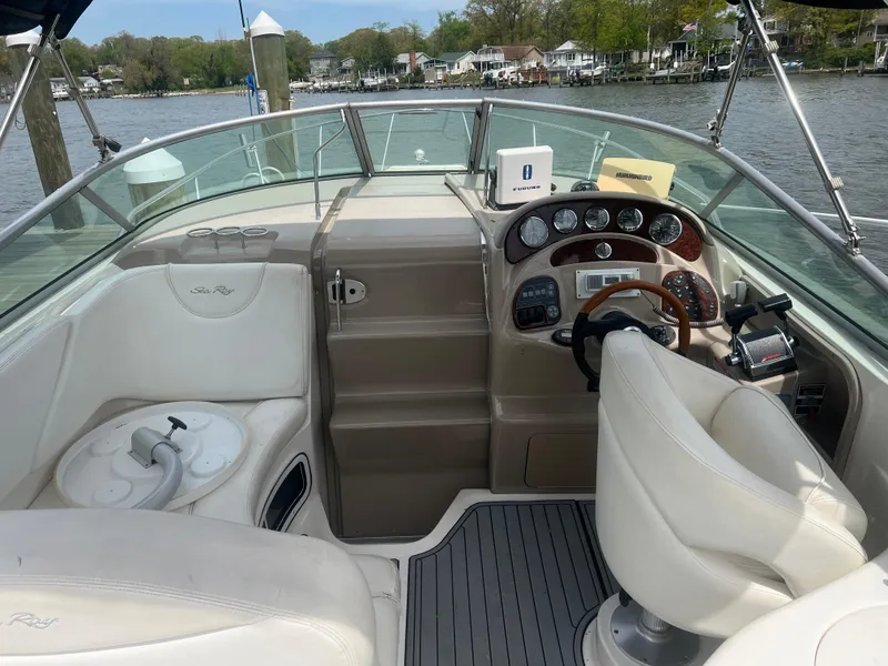 Slide: The Image of 2005 Sea Ray 280 Sundancer boat interior with helm and seating, docked by a scenic river. - 11