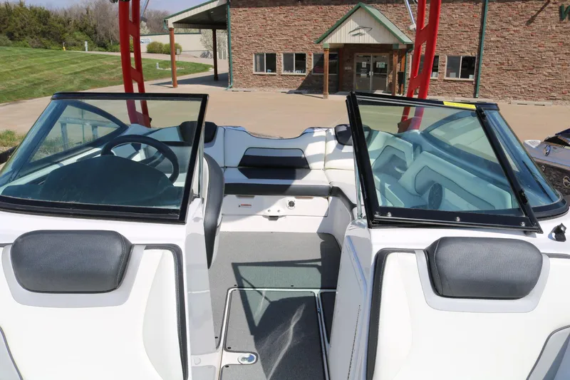 Slide: The Image of 2018 Yamaha Boats AR 195 interior with windshield and seating, parked near a brick building. - 6