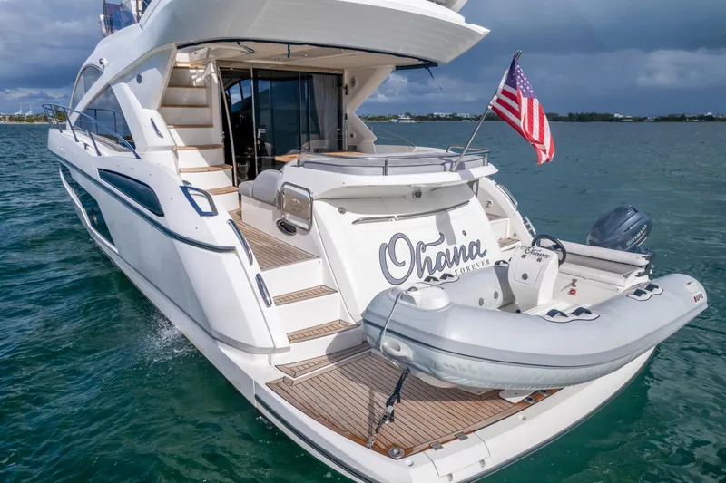 Slide: The Image of 2016 Sunseeker Manhattan 55 yacht with dinghy, American flag, and elegant design on the water. - 16