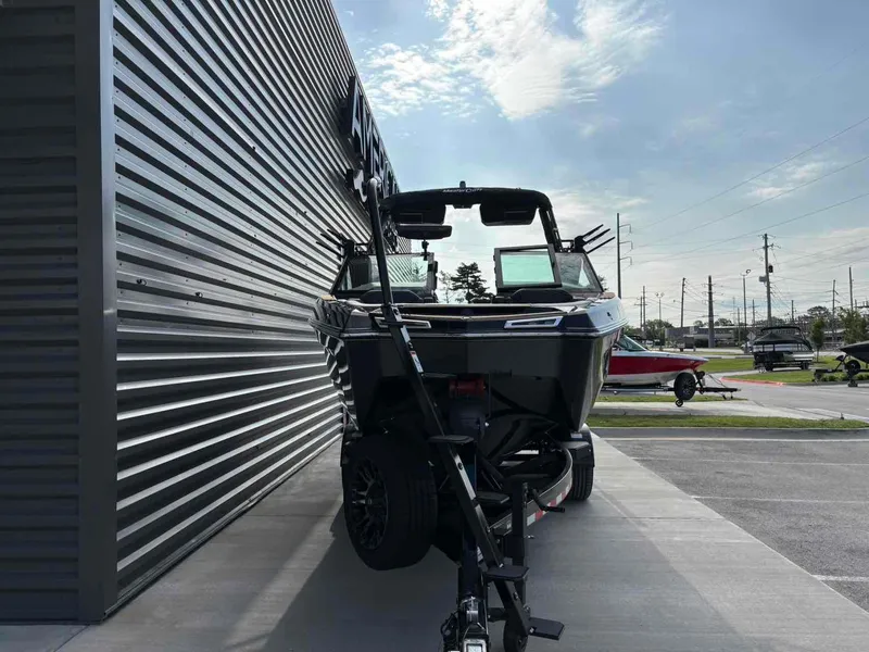 Slide: The Image of 2025 MasterCraft XSTAR23 boat on trailer beside metal building, under a partly cloudy sky. - 3