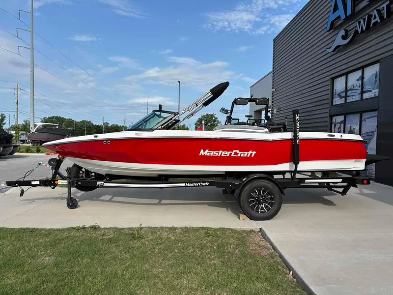 Slide: The Image of 2025 MasterCraft ProStar boat in red and white on a trailer, parked outdoors. - 1