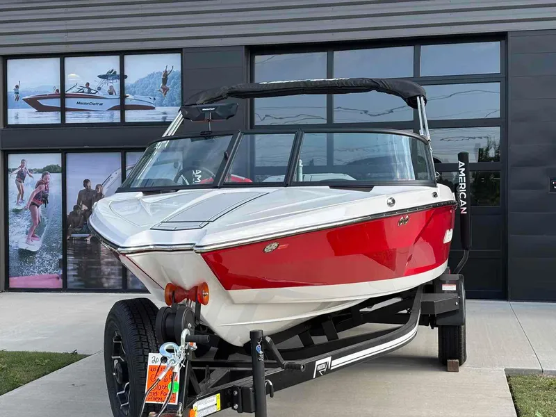 Slide: The Image of 2025 MasterCraft ProStar boat in red and white on a trailer, parked outside a showroom. - 2