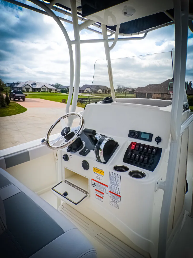 Slide: The Image of 2025 Mako 214CC boat console with steering wheel and controls, parked in a residential area. - 5