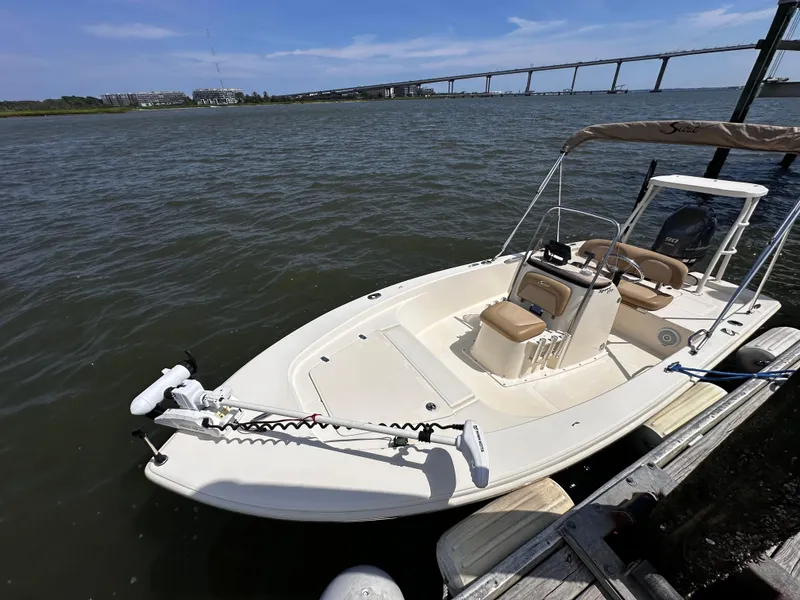 Slide: The Image of 2020 Scout 177 Sport boat docked by a scenic waterfront with a bridge in the background. - 6