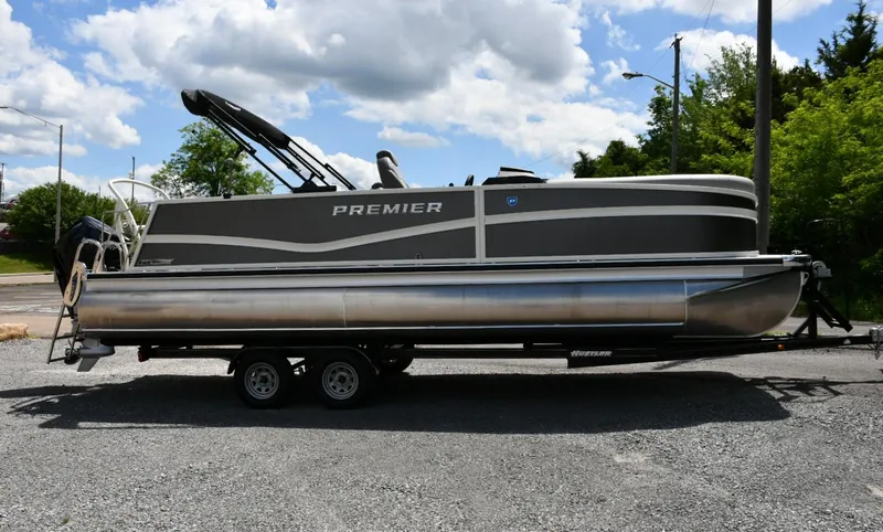 Slide: The Image of 2024 Premier 250 Solaris pontoon boat on trailer, parked outdoors under cloudy sky. - 1