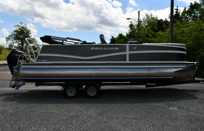 Slide: The Image of 2024 Premier 250 Solaris pontoon boat on trailer, parked outdoors under a cloudy sky. - 2
