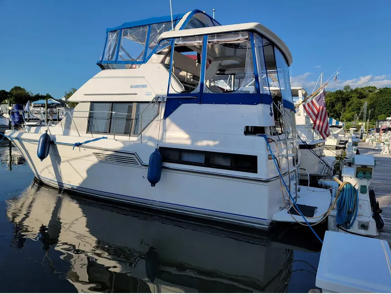 The Image of 1992 Carver 33 Aft Cabin yacht docked in a marina, featuring blue accents and an American flag. - 0