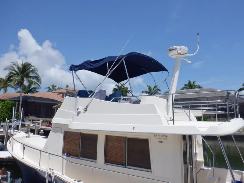 Slide: The Image of 2006 Mainship 34 Trawler with blue canopy docked near palm trees. - 16